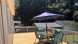 A wooden deck with a table and chairs, a purple umbrella, and a view of a lake.
