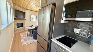 Una cucina moderna con frigorifero integrato, forno a microonde e piano cottura. Presenta un camino in pietra e un'area pranzo con tavolo e sedie.
