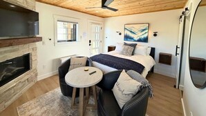 Una camera da letto moderna con soffitto in legno, un camino, un letto con un dipinto di montagna e un piccolo tavolino rotondo.