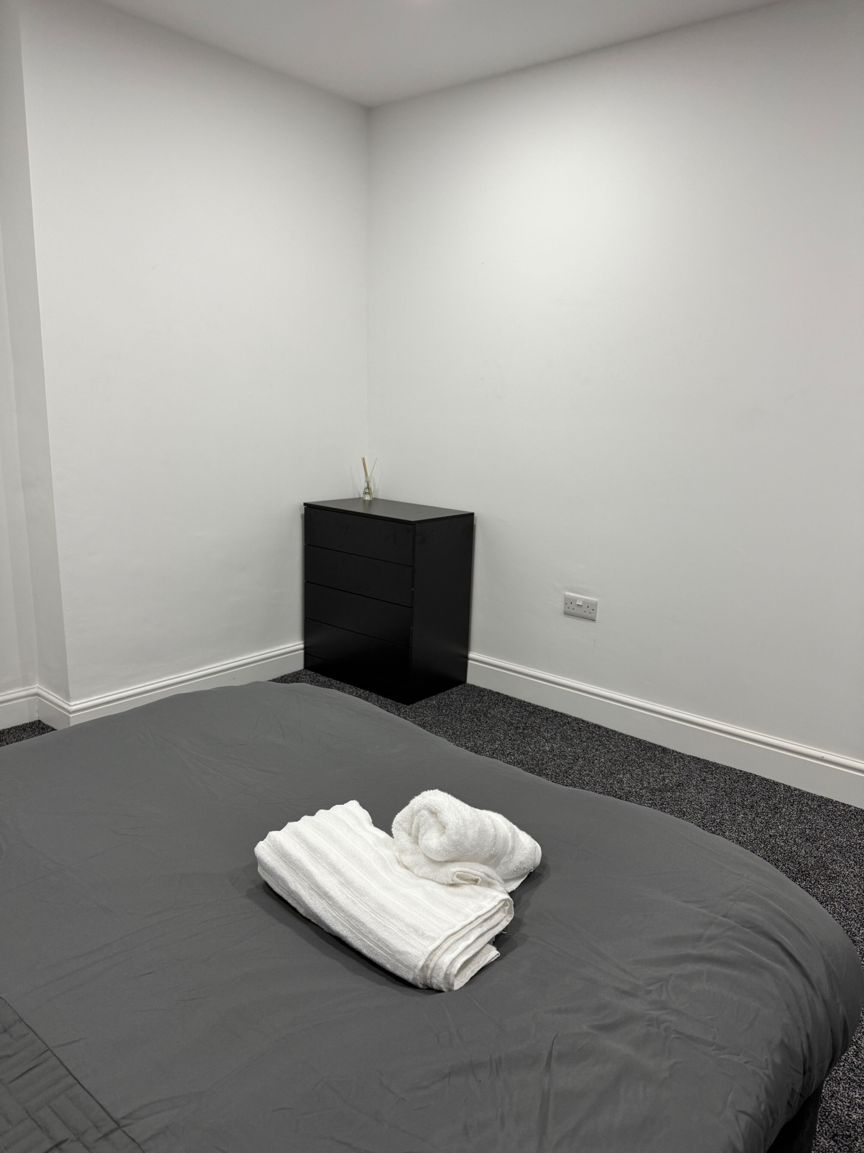 A bedroom with a large bed, a black nightstand, and a white towel on the bed.