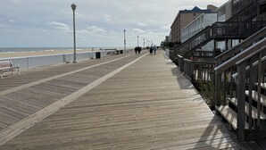 Une promenade en bois menant à une plage, avec une rambarde d’un côté et des bâtiments de l’autre.