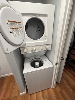 Un appareil compact combinant lave-linge et sèche-linge, doté d’un panneau de commande, d’une étiquette d’avertissement et d’une porte.