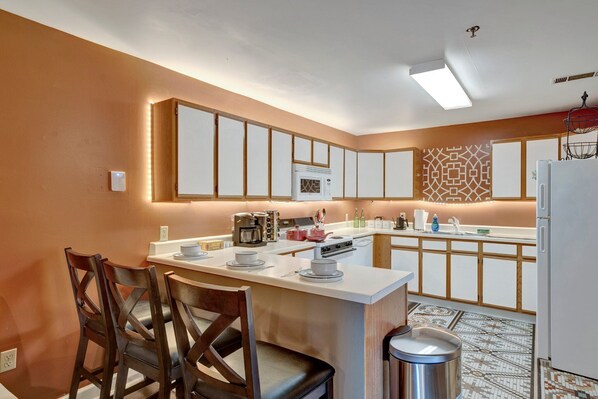 A modern kitchen with a central island, wooden chairs, a microwave, and a patterned backsplash. - Spacious 4-BR Apt, Fast WiFi in Downtown Memphis. Walk to Convention Center. (Memphis)