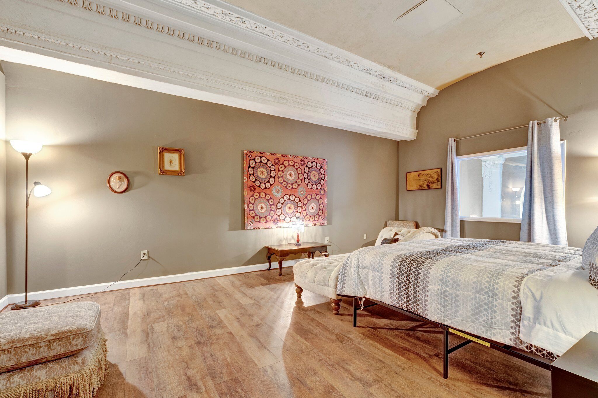 A bedroom with a bed, bedside tables, a floor lamp, and a large tapestry on the wall.