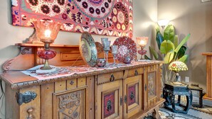 Un aparador de madera con intrincados grabados, un tapiz colorido y diversos objetos decorativos, incluyendo cristalería y una lámpara.