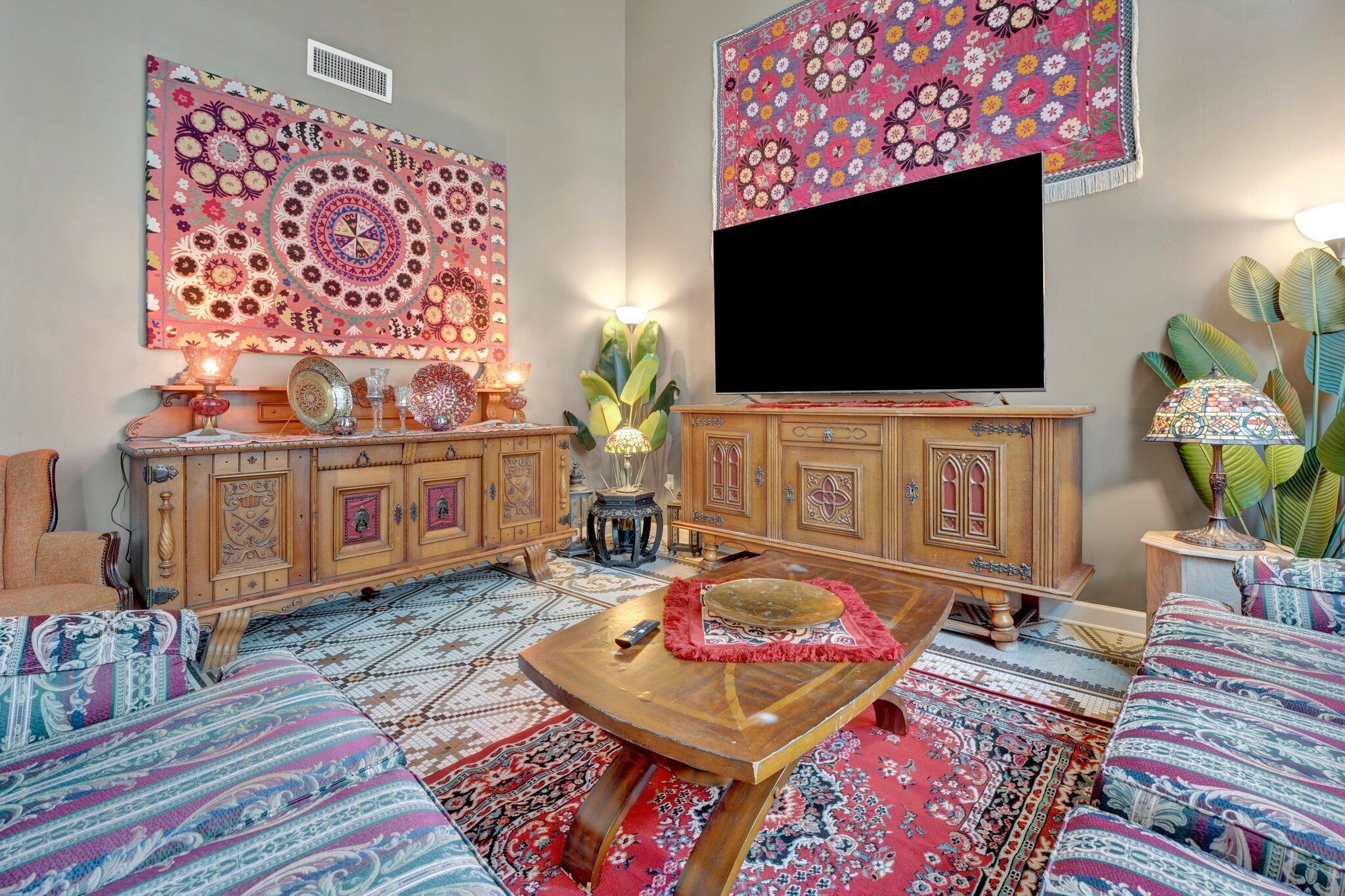 Un salón tradicional con televisor, muebles de madera, alfombras estampadas y elementos decorativos.