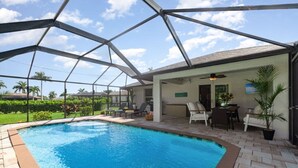 A swimming pool with a covered patio area, outdoor seating, and a view of the surrounding landscape.