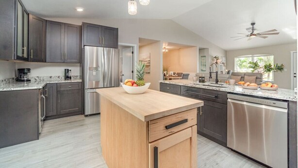 A modern kitchen with dark cabinets, stainless steel appliances, a wooden island, and a dining area with a view.