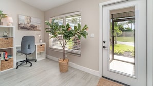 A modern home office with a desk, office chair, and a large potted plant.