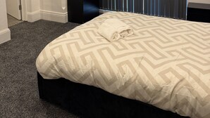 Una habitación de hotel moderna con una cama grande, una mesita de noche oscura, un escritorio integrado y un amplio ventanal con persianas verticales.