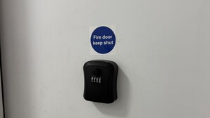 Una puerta blanca con un letrero que indica 'mantener puerta cortafuegos cerrada' y un sistema de intercomunicación negro.