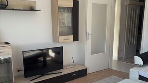 A modern living room with a flat-screen TV, a wooden cabinet, a white door, and a white table. - Apartment Meskovic Tuzla (Tuzla Grad)