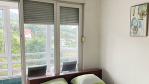 A bedroom with a bed, a window with blinds, a chair, and a painting on the wall. - Apartment Meskovic Tuzla (Tuzla Grad)