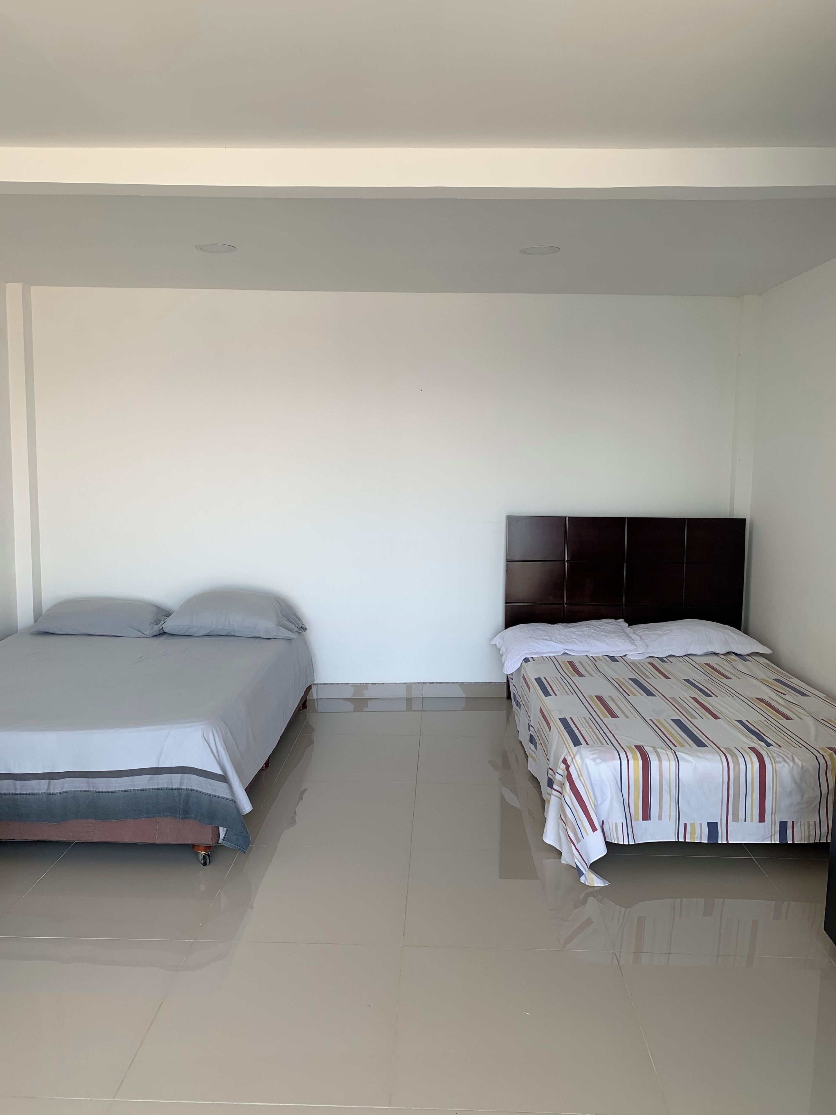 A room with two beds, one with a dark headboard and the other with a patterned bedspread.