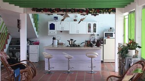 A kitchen with white cabinets, a central island with stools, and a hanging bird feeder. - VILLA NINA. Enjoy the most beautiful sunsets. (Manizales)