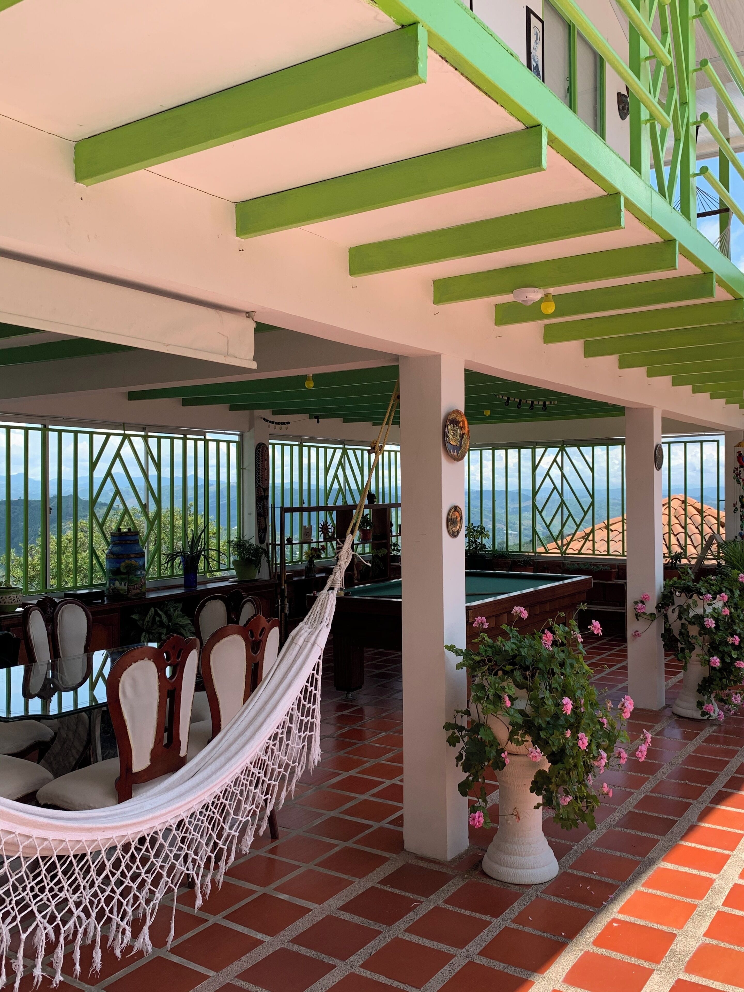 A covered outdoor area with a pool table, chairs, a hammock, and potted plants.