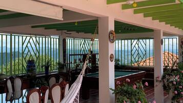 A covered outdoor area with a pool table, chairs, a hammock, and potted plants.