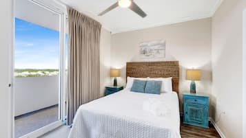 A bedroom with a bed, two bedside tables with lamps, a ceiling fan, a view through a sliding door, and a painting on the wall.