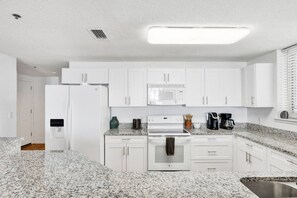 Une cuisine moderne avec des meubles blancs, un plan de travail en granit, un four à micro-ondes, une cuisinière et une machine à café.