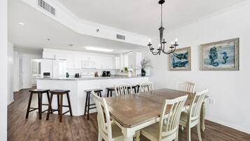 A spacious kitchen with white cabinetry, a central island, and a dining area with a wooden table and white chairs.