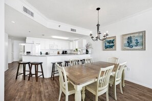 Une cuisine spacieuse avec des meubles blancs, un îlot central et un coin repas comprenant une table en bois et des chaises blanches.
