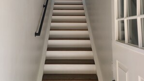Una escalera con paredes blancas y detalles de madera, que conduce a una puerta con ventana.