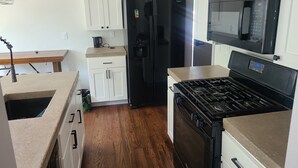 Una cocina con armarios blancos, un refrigerador negro, un microondas, una estufa y una cafetera.