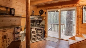 Een houten chalet van binnen met een keuken, een glazen schuifdeur naar een terras en een houten trap.