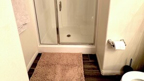 A bathroom with a glass-enclosed shower, a toilet, and two rugs on the floor.
