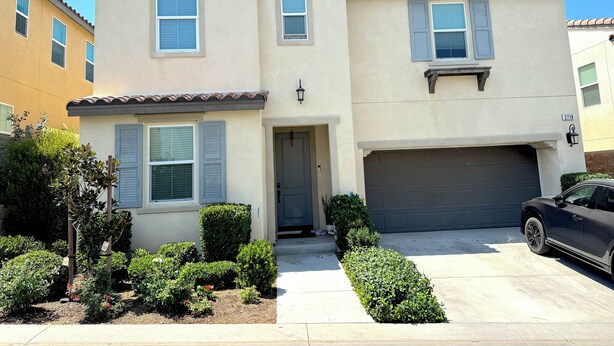 A two-story house with a garage, a driveway, and a well-maintained garden with various shrubs and flowers.