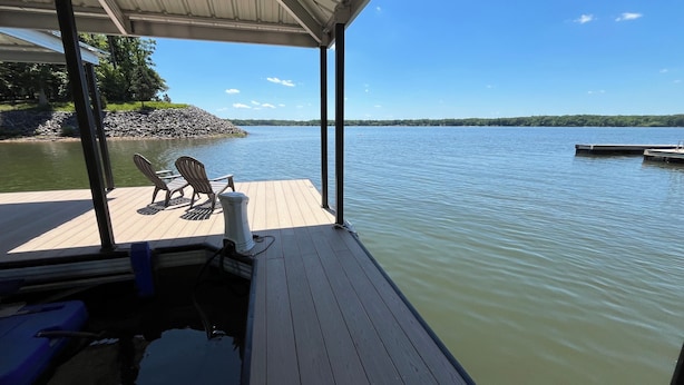 Eine Holzterrasse mit Stühlen und Tisch, mit Blick auf einen ruhigen See, im Hintergrund ein Steg.