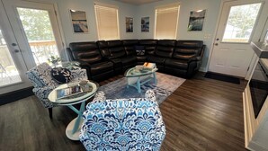 Ein Wohnzimmer mit Ecksofa, Glastisch, gemusterten Sessel und einem Esstisch.
