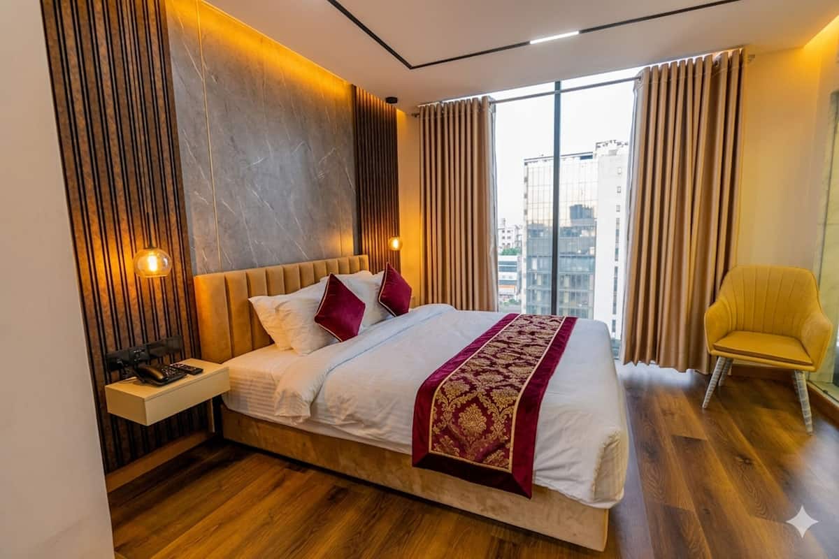 Ein modernes Hotelzimmer mit einem großen Bett, einem Nachttisch mit Telefon, einem Sessel und Blick auf die Stadt durch große Fenster.