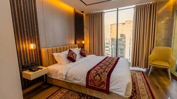 A modern hotel room with a large bed, a bedside table, a chair, and a view of the city.