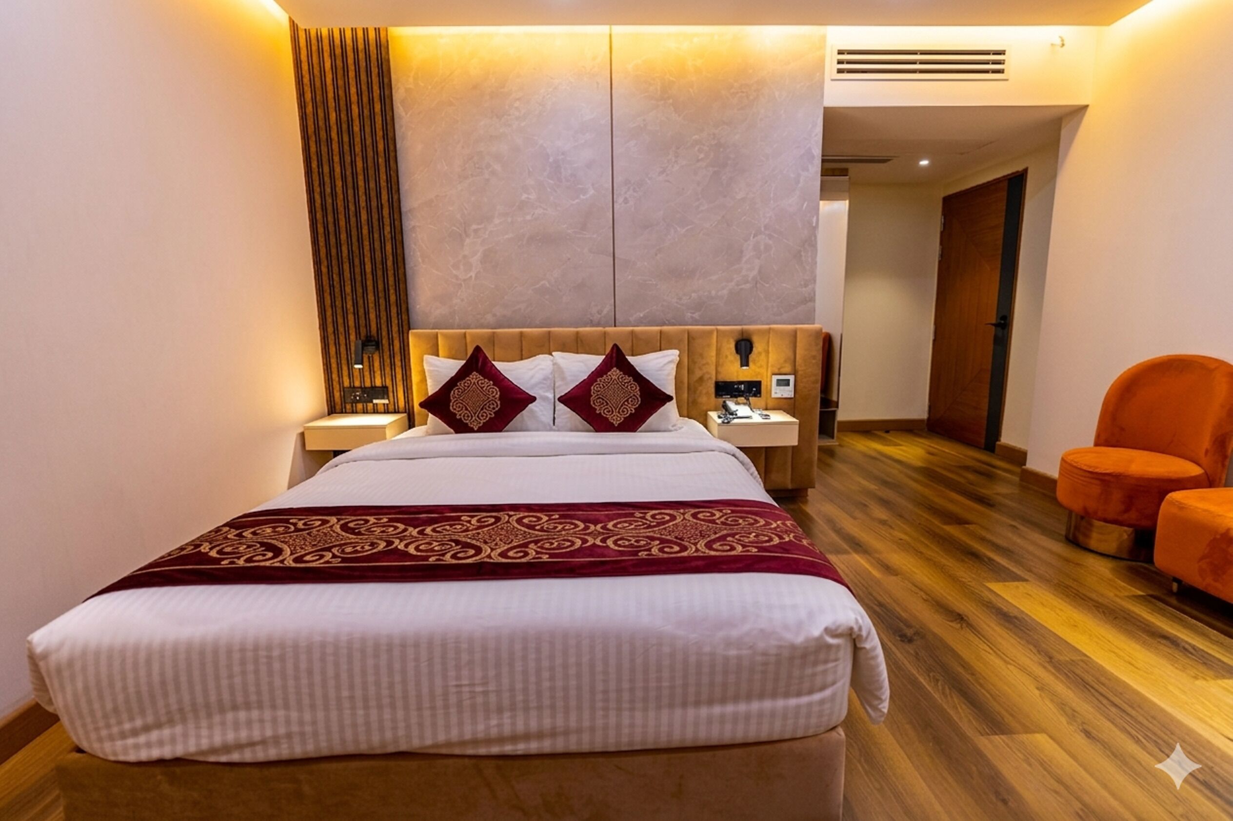Una camera d'albergo con un letto, comodini, pavimento in legno e una poltrona arancione.