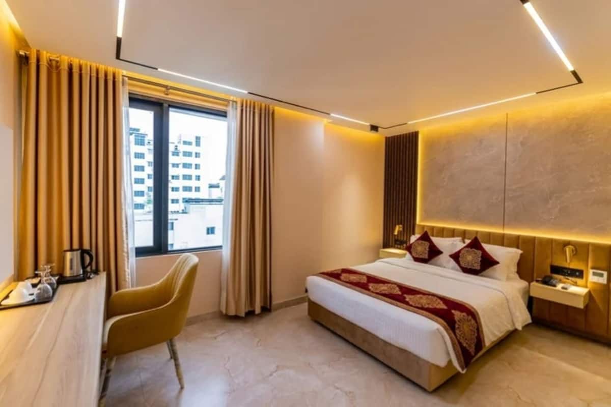 Ein Hotelzimmer mit Bett, Schreibtisch, Stuhl, Nachttisch und einem Fenster mit Vorhängen.