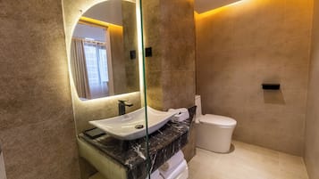 Et moderne badeværelse med et glasafskærmet håndvask, en marmor bordplade, et hvidt toilet og et stort spejl.