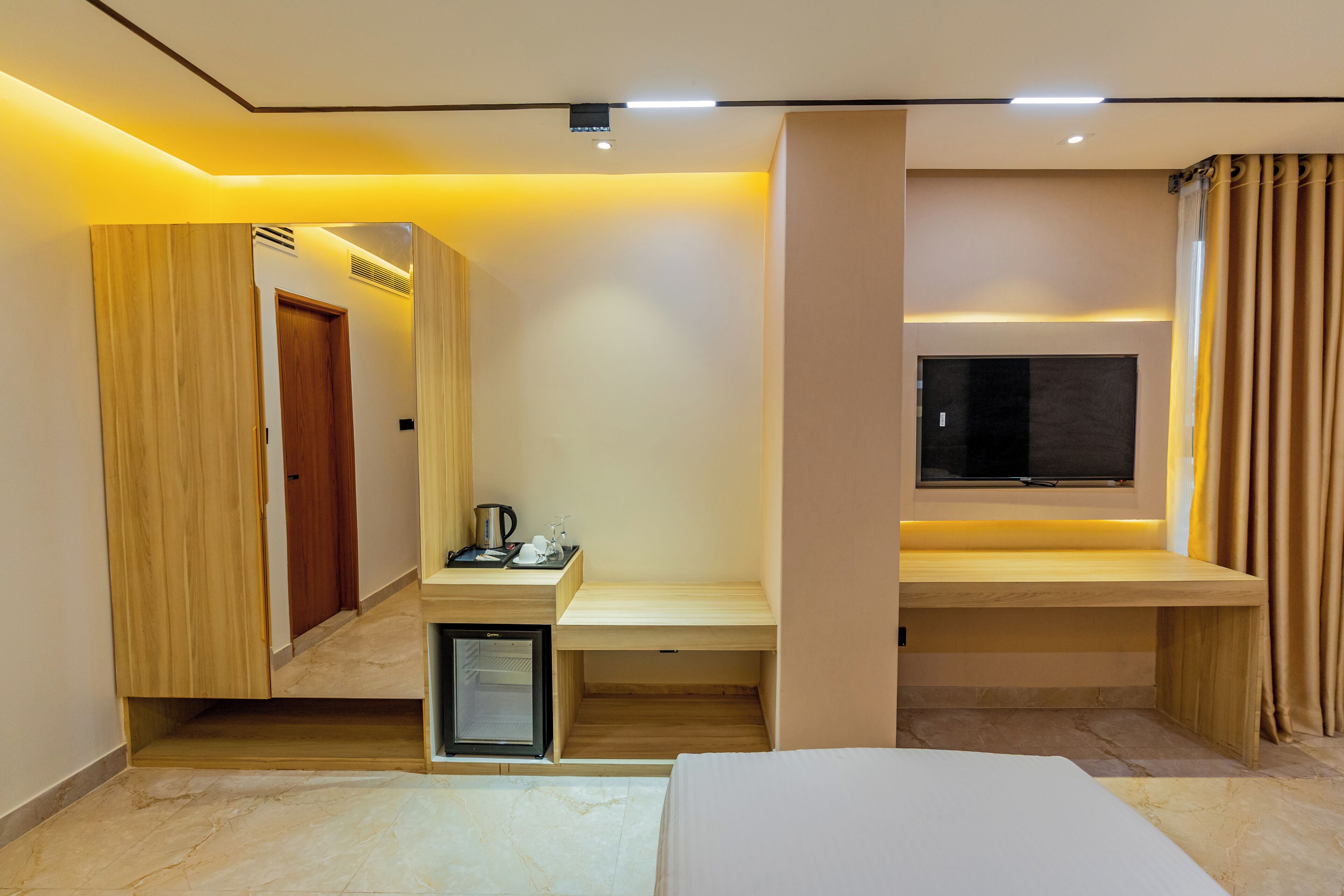 A modern hotel room with a bed, a desk, a television, and a minibar.