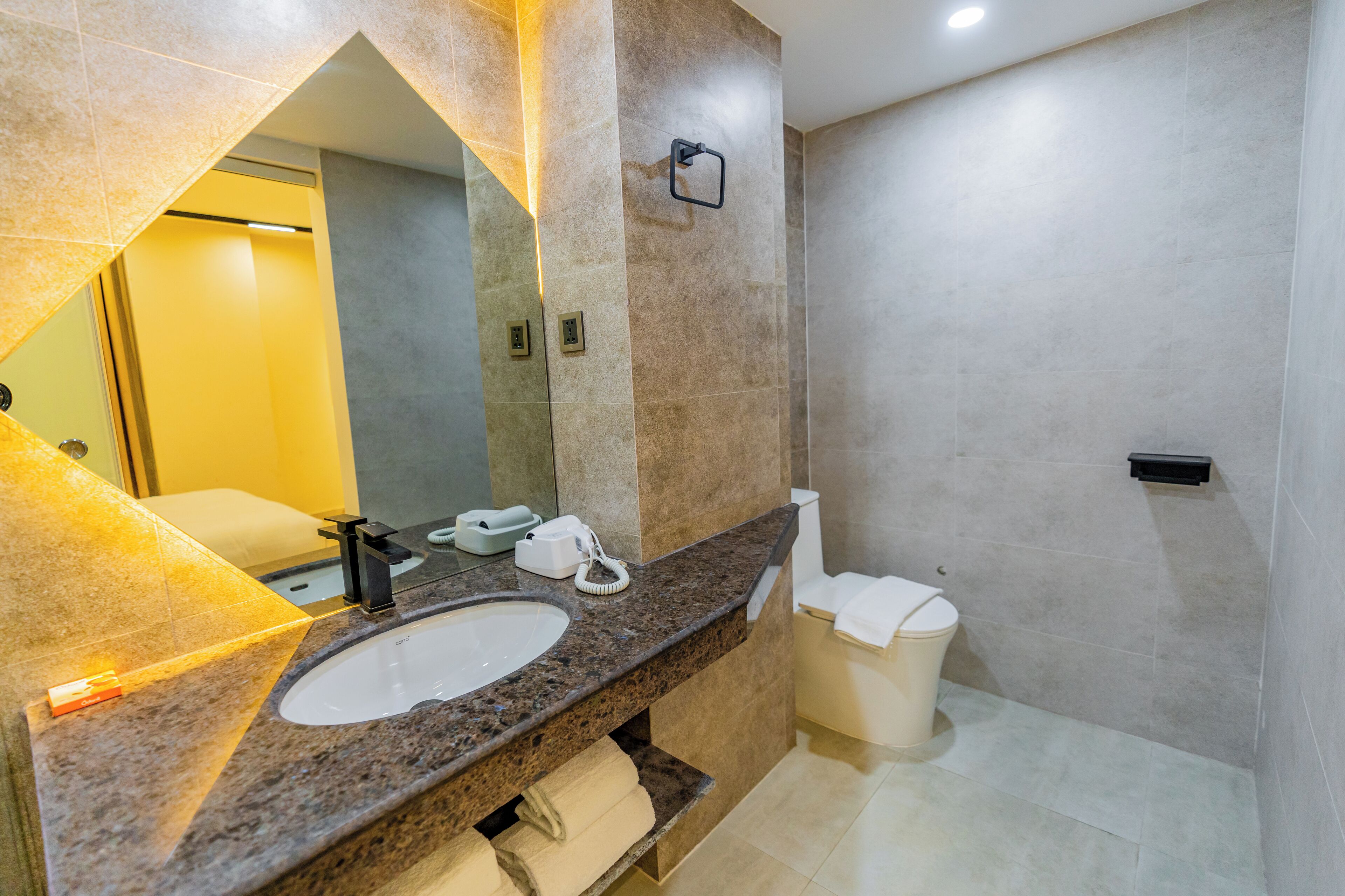 A modern bathroom with a granite countertop, a white sink, a mirror, a toilet, and a towel rack.