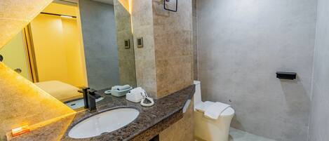 A modern bathroom with a granite countertop, a white sink, a mirror, a toilet, and a towel rack.