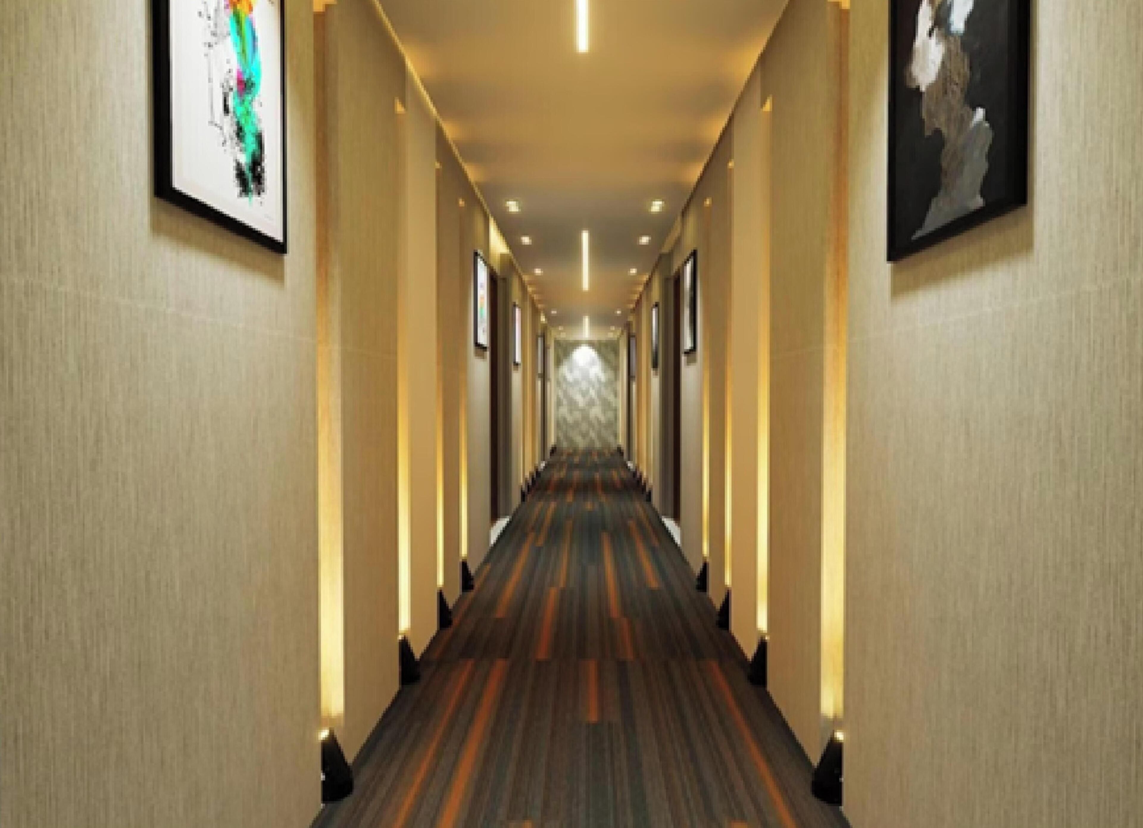 Een hotelgang met tapijtvloer, kunstwerken aan de muur en inbouwverlichting.