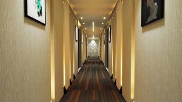 A hotel hallway with a carpeted floor, framed artwork on the walls, and recessed lighting.