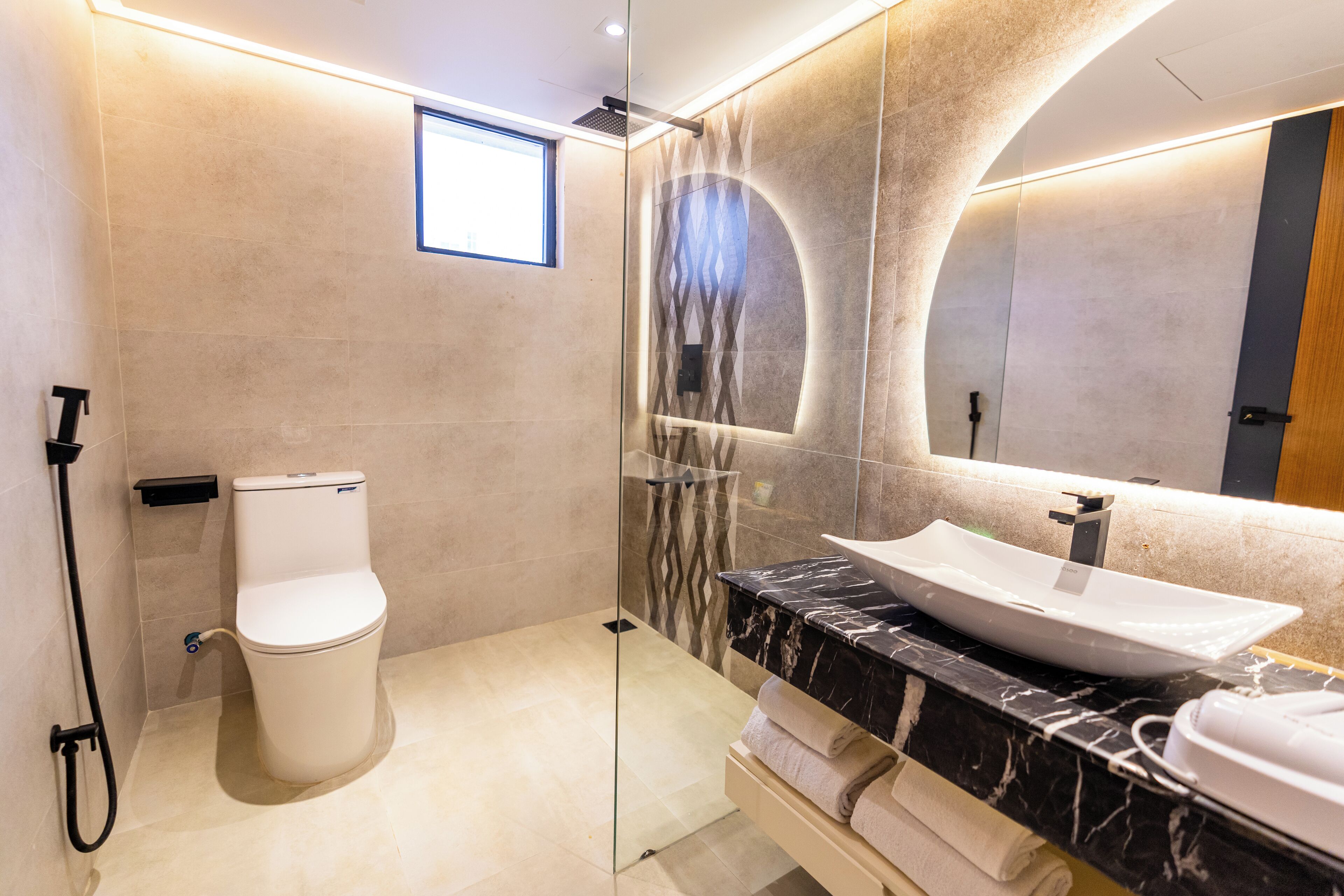 Un baño moderno con ducha envuelta en vidrio, inodoro blanco y tocador de mármol con lavamanos.