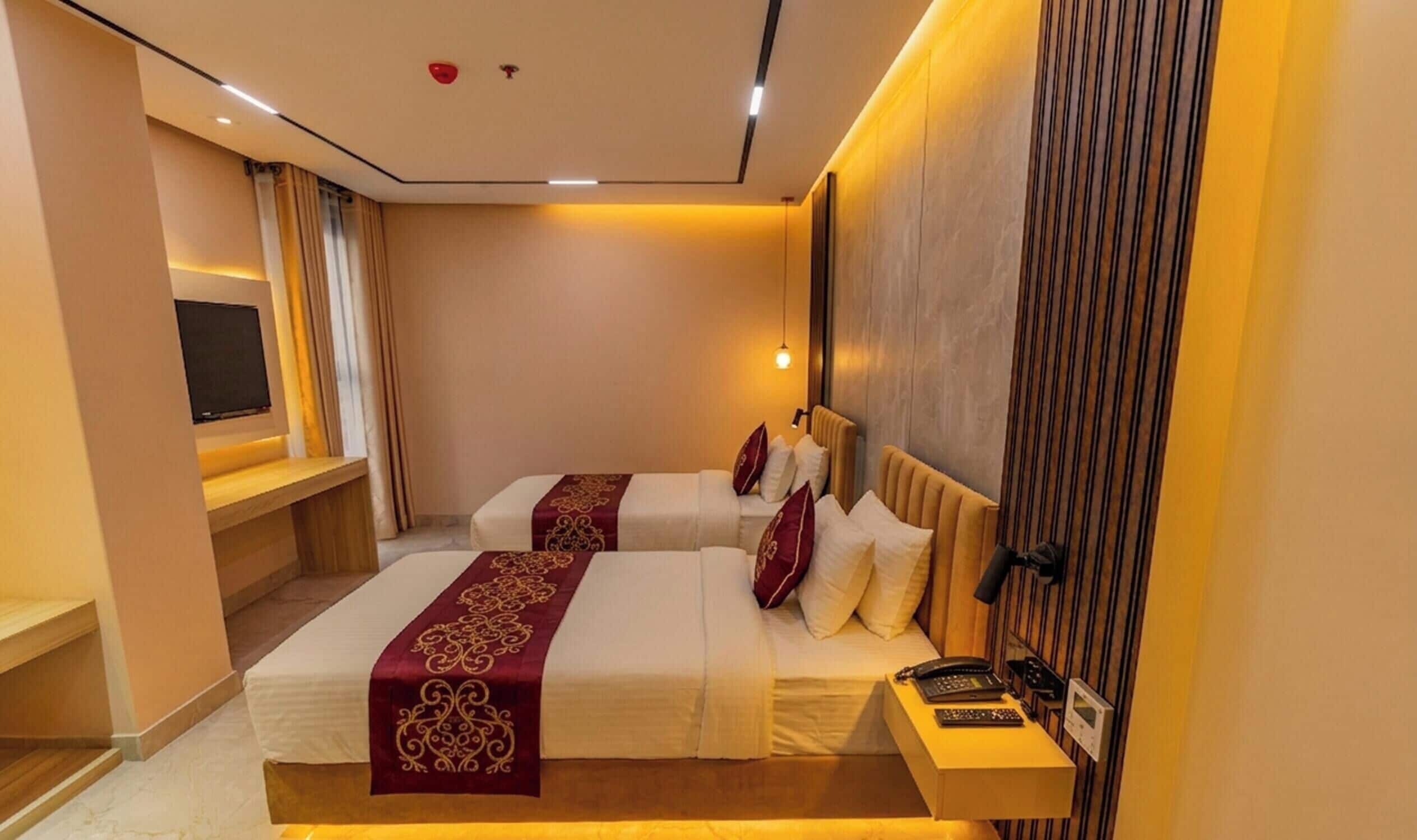 Une chambre d’hôtel avec deux lits, une télévision, une table de chevet avec un téléphone et une lampe fixée au mur.