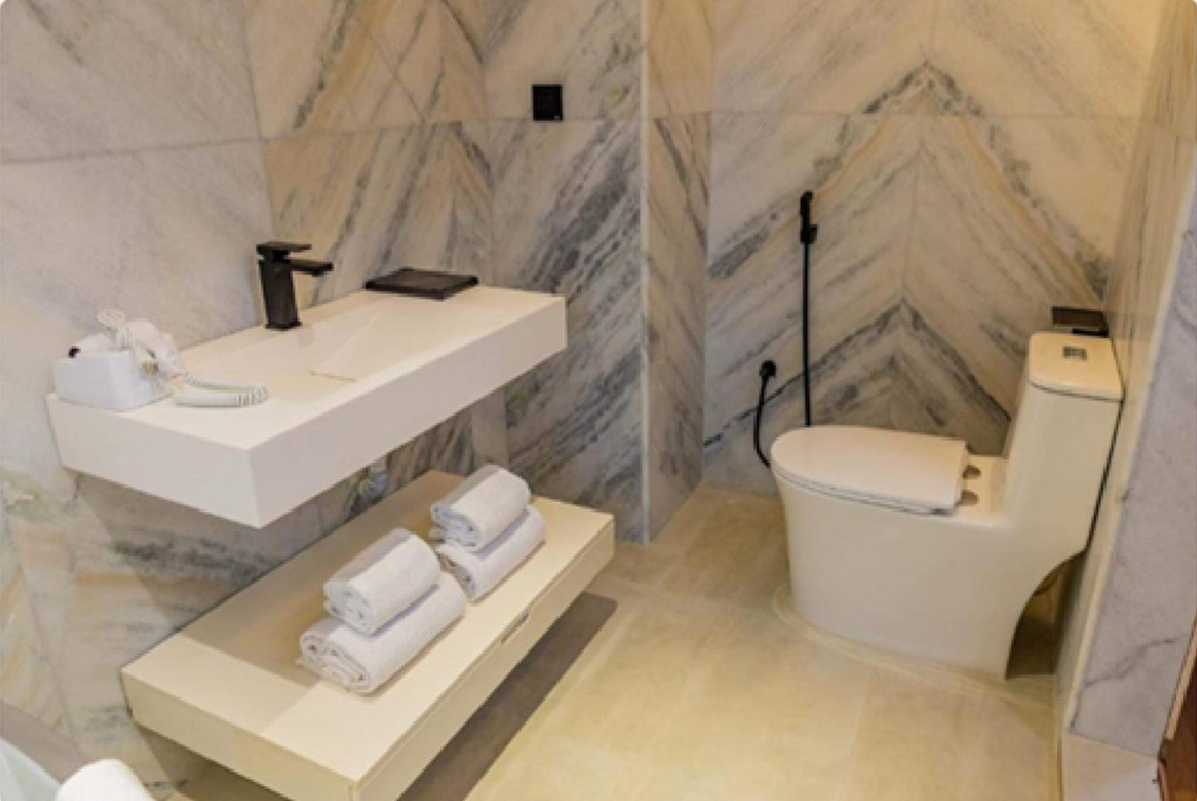 A bathroom with a marble wall, a white sink with a towel rack, and a toilet.