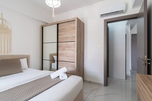 A modern hotel room with a bed, a wooden wardrobe, a mirror, and an air conditioning unit. - Infinity 1-Bedroom Apartment in Larnaca (Larnaca)