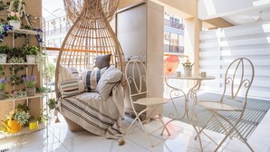 A cozy indoor seating area with a wicker hanging chair, a cushioned bench, and a small round table. - Infinity 1-Bedroom Apartment in Larnaca (Larnaca)