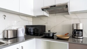 A modern kitchen with white cabinets, a stainless steel toaster, a coffee maker, a microwave, and a pot on the stove. - Infinity 1-Bedroom Apartment in Larnaca (Larnaca)