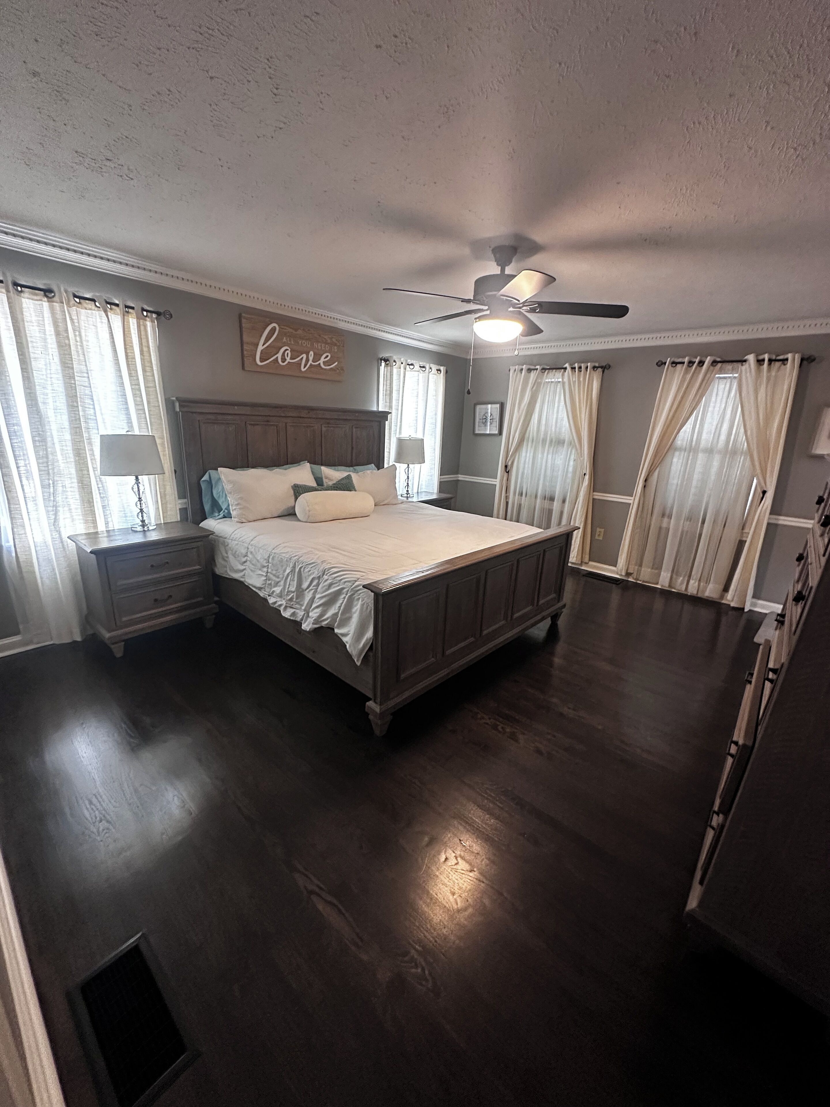 Un dormitorio con una cama grande, ventilador de techo y cortinas en las ventanas.