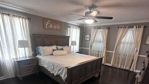 Ein Schlafzimmer mit einem großen Bett, einem Deckenventilator und Vorhängen an den Fenstern.